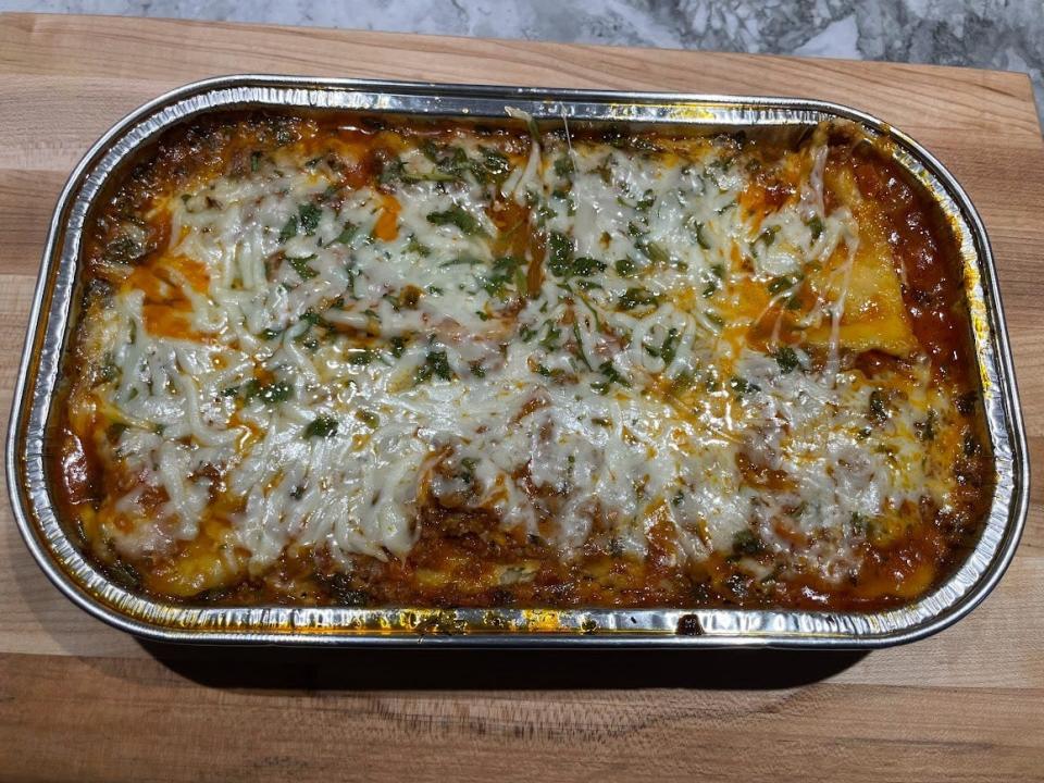 Fully baked ravioli lasagna with melted white and yellow cheese and tomato sauce bubbling up around edges. The tray sits on a wooden cutting board