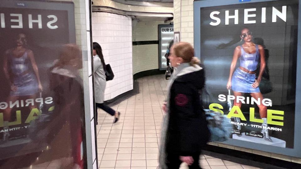 A woman walks past a Shein sale advert in an underground station