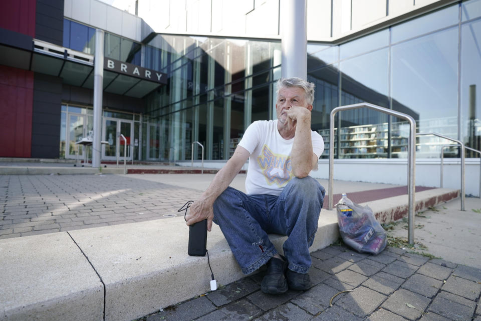 Jerry Frajman sits in front of the Cedar Rapids Public Library after charging his cell phone, Friday, Aug. 14, 2020, in Cedar Rapids, Iowa. The storm that struck Monday morning left tens of thousands of Iowans without power as of Friday morning. (AP Photo/Charlie Neibergall)