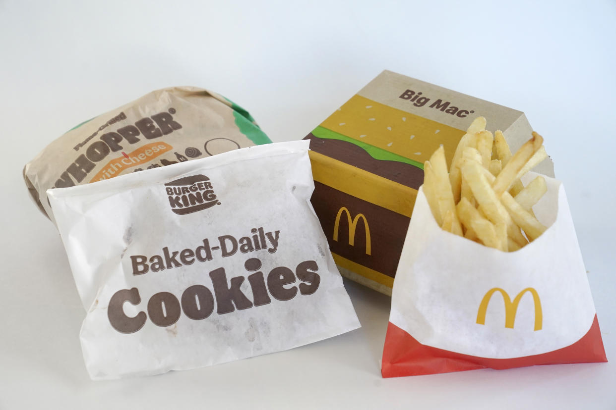 A Burger King Whopper in a wrapper, behind left, and a bag of Burger King cookies, left, rest next to a McDonald's Big Mac in a container, behind right, and a bag of McDonald's fries, in Walpole, Mass., Wednesday, April 20, 2022. Environmental and health groups are pushing dozens of fast food companies, supermarkets chains and other retail outlets to remove PFAS from their packaging. (AP Photo/Steven Senne)