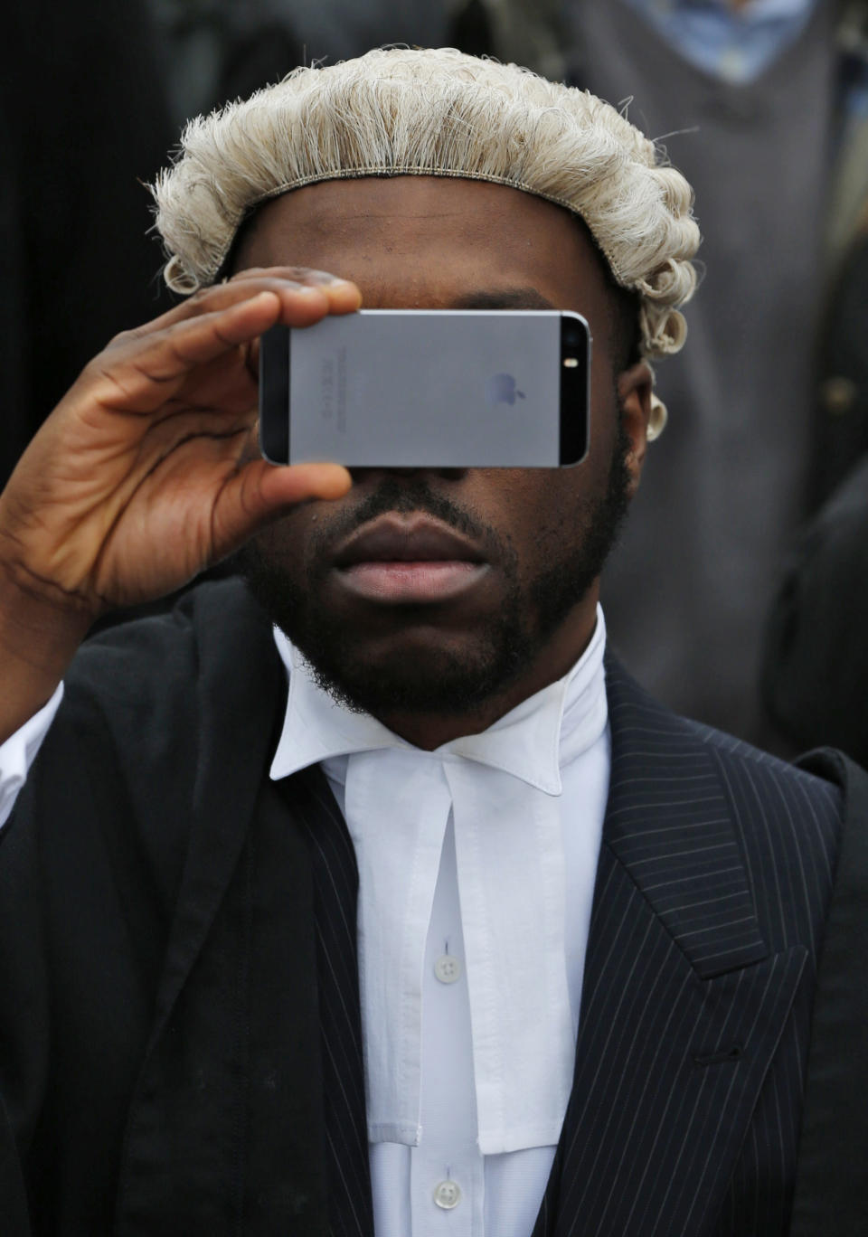 A lawyer in his full court dress of wig and gown, uses his mobile phone to take a picture as he participates in a rally to protest against legal aid cuts, across from the Houses of Parliament in central London, Friday, March 7, 2014. The protest coincides with a nationwide demonstration of non-attendance of lawyers which will affect hundreds of cases across the country. (AP Photo/Lefteris Pitarakis)