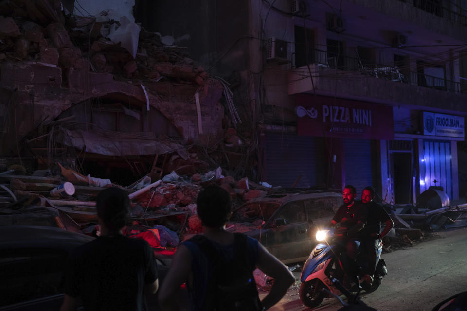 People ride past damaged buildings at a neighborhood without electricity near the scene of Tuesday's explosion that hit the seaport of Beirut, Lebanon, Friday, Aug. 7, 2020. Rescue teams were still searching the rubble of Beirut's port for bodies on Friday, nearly three days after a massive explosion sent a wave of destruction through Lebanon's capital, killing over a hundred people and wounding thousands. (AP Photo/Felipe Dana)