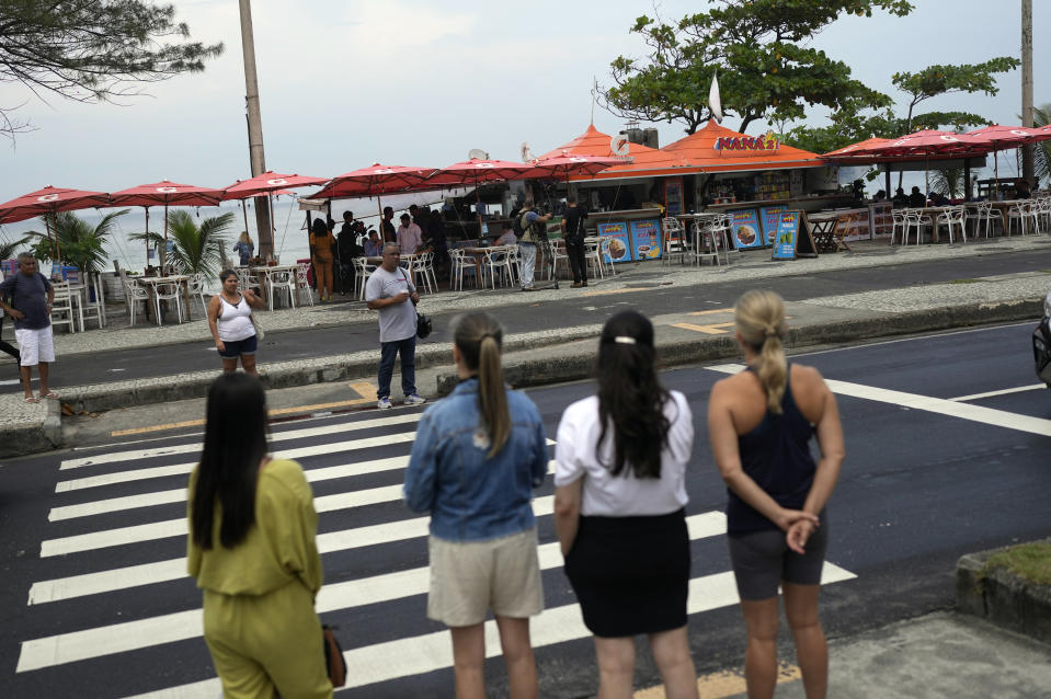 Pedestrians stand across the street from the food and bar kiosk "Nana 2" on the beach in the Barra de Tijuca neighborhood of Rio de Janeiro, Brazil, Thursday, Oct. 5, 2023. Three of four doctors who were shot overnight at the bar have died. (AP Photo/Silvia Izquierdo)