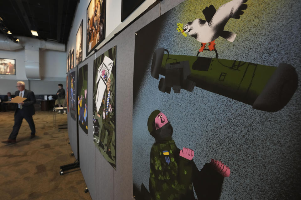 Gary Bouchard, a professor at Saint Anselm College, left, passes by posters by Ukrainian artists during the opening of an art exhibit called "Our Fire is Stronger Than Your Bombs" at Saint Anselm College, in Manchester, N.H., Monday, May 1, 2023. The art exhibit marking the one-year anniversary of the Russian invasion of Ukraine features new work by Ukrainian illustrators, some of whom have been living without electricity or water. The poster "Weapons for Ukraine" by Anna Sarvira hangs at right. (AP Photo/Steven Senne)