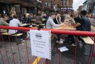 Members of the public are seen at a bar in Manchester's Northern Quarter, England, Saturday July 4, 2020. England is embarking on perhaps its biggest lockdown easing yet as pubs and restaurants have the right to reopen for the first time in more than three months. In addition to the reopening of much of the hospitality sector, couples can tie the knot once again, while many of those who have had enough of their lockdown hair can finally get a trim. (AP Photo/Jon Super)