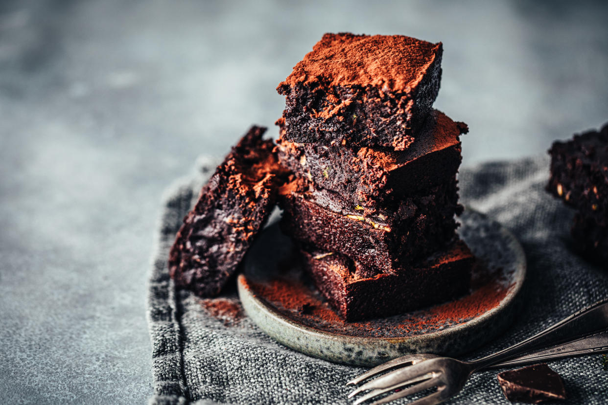 Pile of freshly made chocolate zucchini brownies garnished with cocoa powder on a round wooden plate. Delicious chocolate zucchini brownies served.