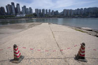 Cones and caution tape block a path leading to the Yangtze River in southwestern China's Chongqing Municipality, Friday, Aug. 19, 2022. Ships crept down the middle of the Yangtze on Friday after the driest summer in six decades left one of the mightiest rivers shrunk to barely half its normal width and set off a scramble to contain damage to a weak economy in a politically sensitive year. (AP Photo/Mark Schiefelbein)