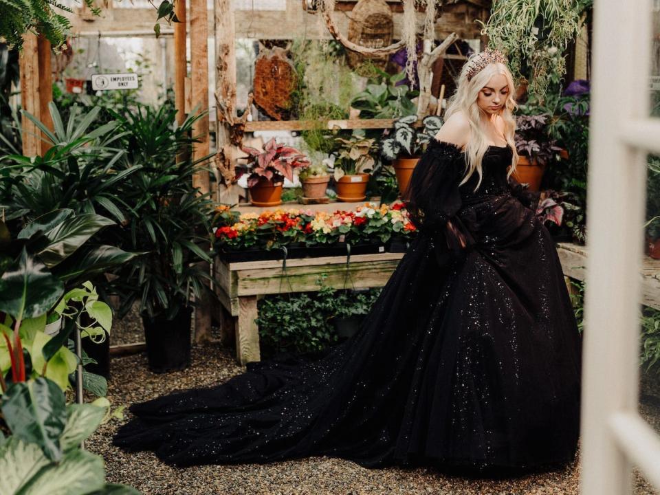 A bride poses in her black wedding dress in a greenhouse.