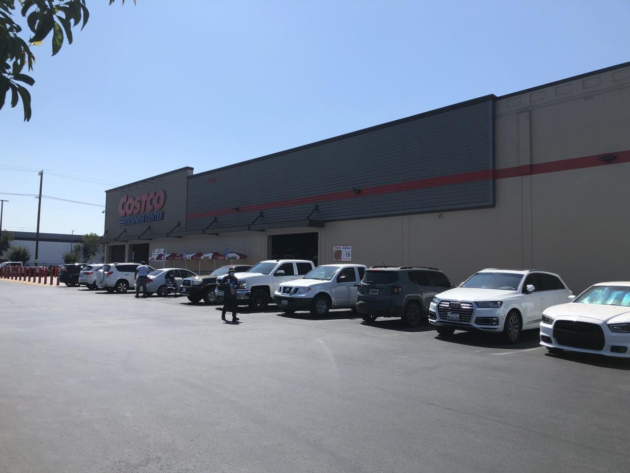 A wider shot of a Costco Business Center exterior with a line of cars parked outside and a couple of patrons in the parking lot.