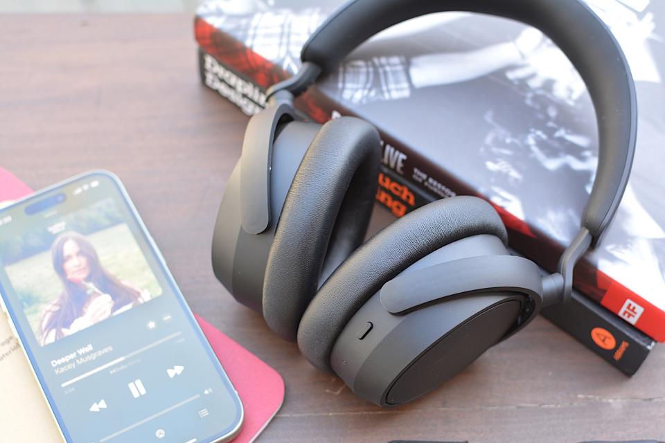 <p>Sennheiser Accentum Plus headphones sitting on a table, propped up by two books with an iPhone playing Kacey Musgraves to the left.</p>
