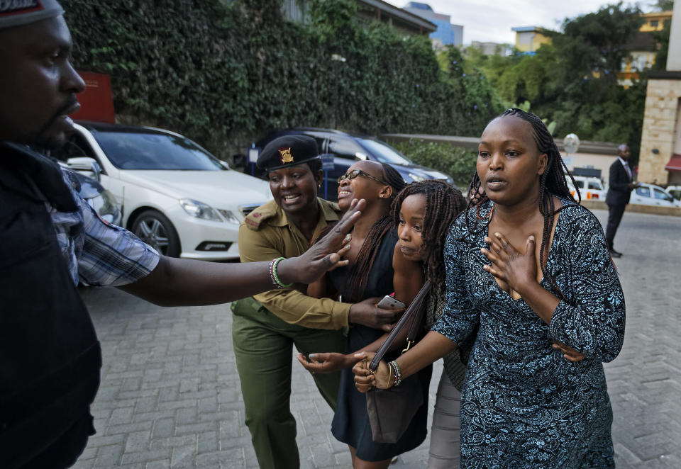 Civilians flee helped by a member of the security forces at a hotel complex in Nairobi, Kenya, Tuesday, Jan. 15, 2019. Terrorists attacked an upscale hotel complex in Kenya's capital Tuesday, sending people fleeing in panic as explosions and heavy gunfire reverberated through the neighborhood. (AP Photo/Ben Curtis)