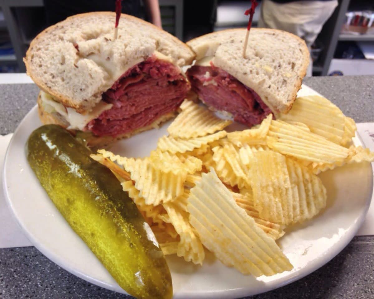 Hear-O Israel Sandwich with ripple potato chips and a pickle slice on a white ceramic plate, Benji's Deli and Restaurant, Milwaukee, on a grey countertop at the restaurant