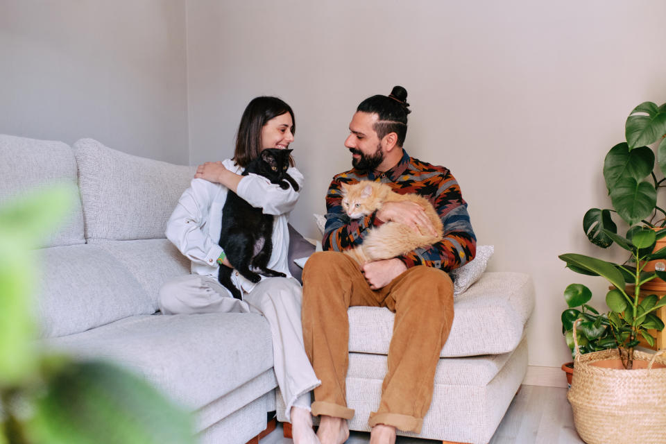 Happy couple hold their two cats sitting on their living room sofa.