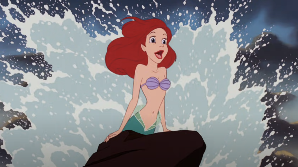 Ariel singing on a rock as waves crash up behind her