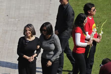 Florinda Meza (L), widow of the late screenwriter Roberto Gomez Bolanos, is accompanied by an unidentified person after leaving a flower on the pitch of the Azteca stadium before the start of a mass held in his honour in Mexico City November 30, 2014. REUTERS/Tomas Bravo