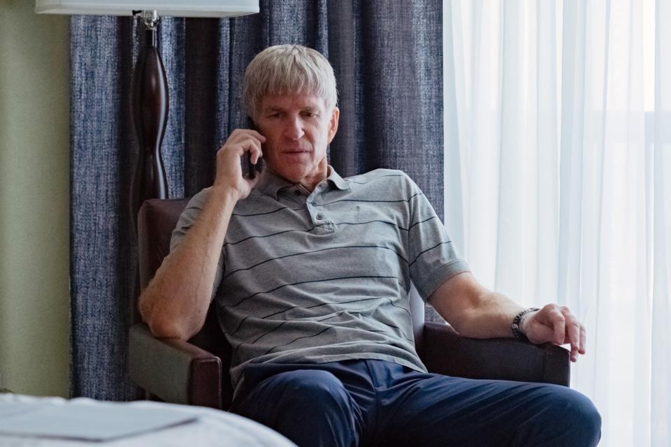 Matthew sitting in a chair and on the phone in a scene from Operation Varsity Blues