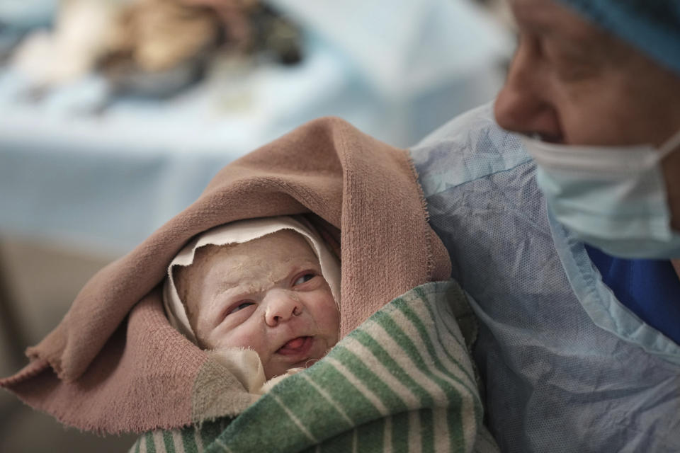 A medical worker holds a newborn baby wrapped in a blanket.