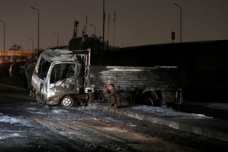 A man sits next to a burned truck following a fire that broke out in?Egypt's Shuqair-Mostorod crude oil?pipeline, at the beginning of Cairo-Ismailia road
