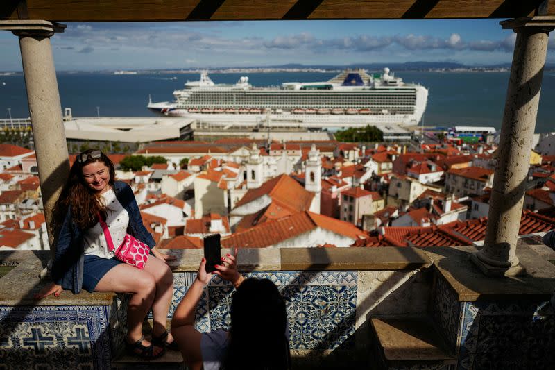 People take pictures in Santa Luzia viewpoint, while a cruise ship prepares to leave from the Cruise Port of Lisbon