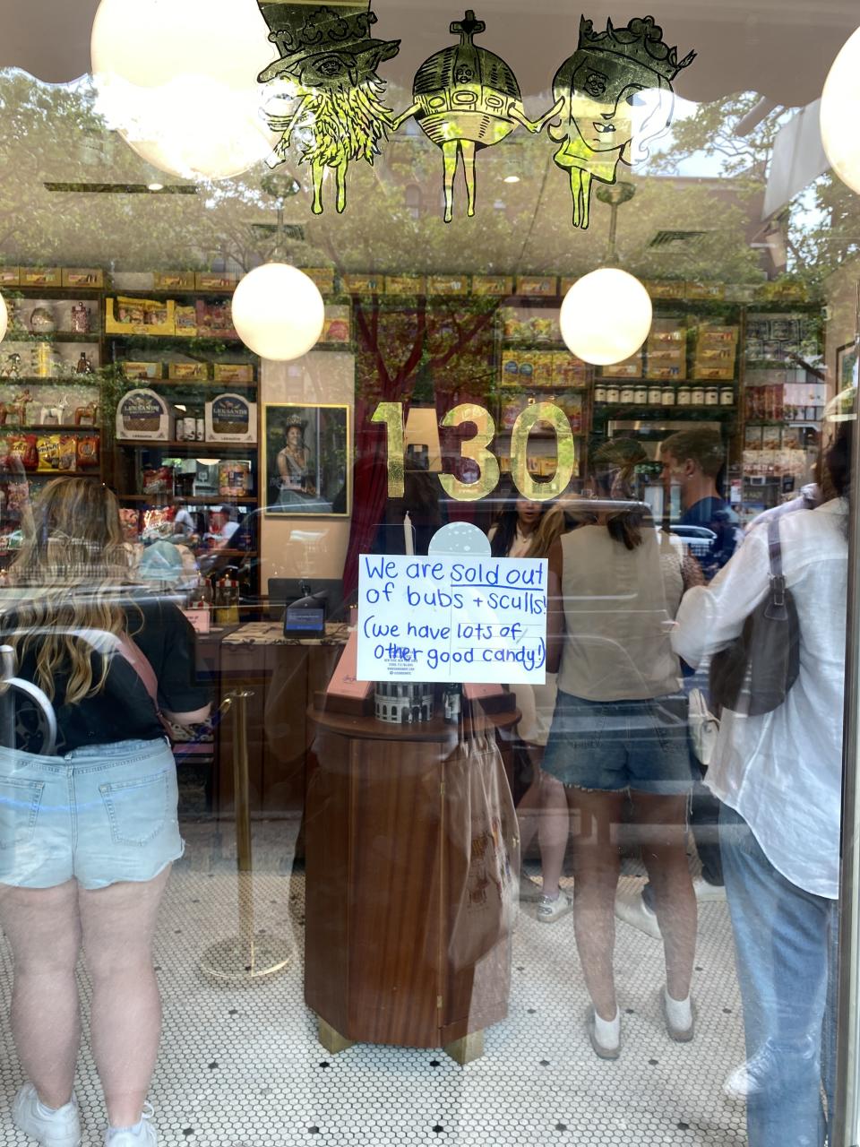 A store window displays a sign reading, "We are sold out of bubs + sculls (we have lots of other good candy)," with people inside shopping