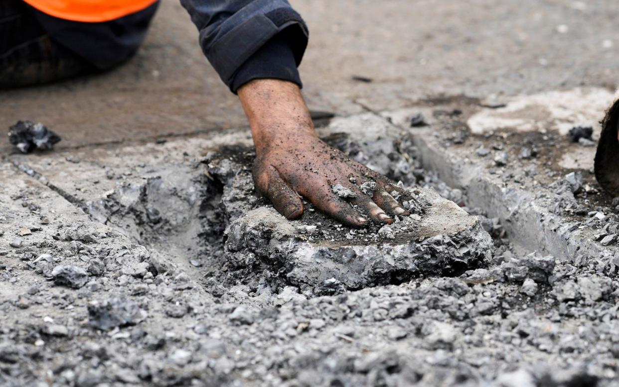 Police remove asphalt next to the hand of a climate activist who glued himself to a road in Berlin on Monday - Markus Schreiber/AP