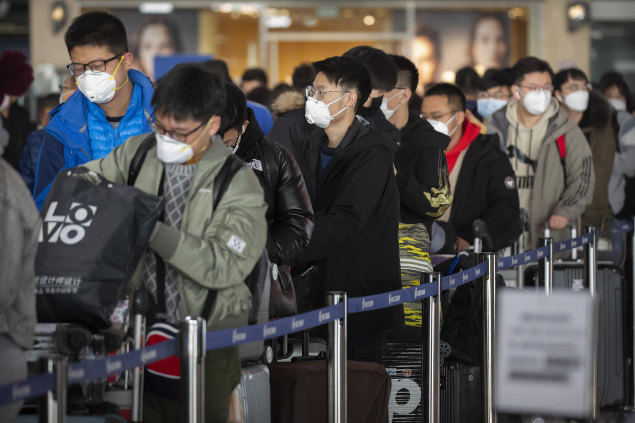 Travelers wearing face masks line up at the Air China check-in counters at Beijing Capital International Airport in Beijing, Friday, March 6, 2020. An industry group says the spreading coronavirus could cost airlines as much as $113 billion in lost revenue. (AP Photo/Mark Schiefelbein)