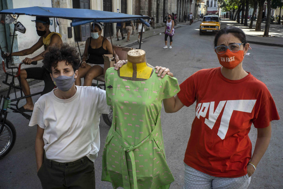 Idania Del Río, left, and Leire Fernández, owners of Clandestina, pose with a mannequin dressed in clothes they created, outside their store in Havana, Cuba, Feb. 18, 2021. Tourists poured through their shop until the Trump administration turned off the taps that had been opened just a few years before by then-President Barack Obama. Today, the doors swing open less often, with tourism choked both by U.S. sanctions meant to punish Cuba's government and a pandemic that has squashed tourism almost everywhere. (AP Photo/Ramon Espinosa)