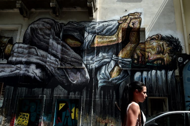 A woman passes by graffiti depicting a homeless person in central Athens on July 11, 2015