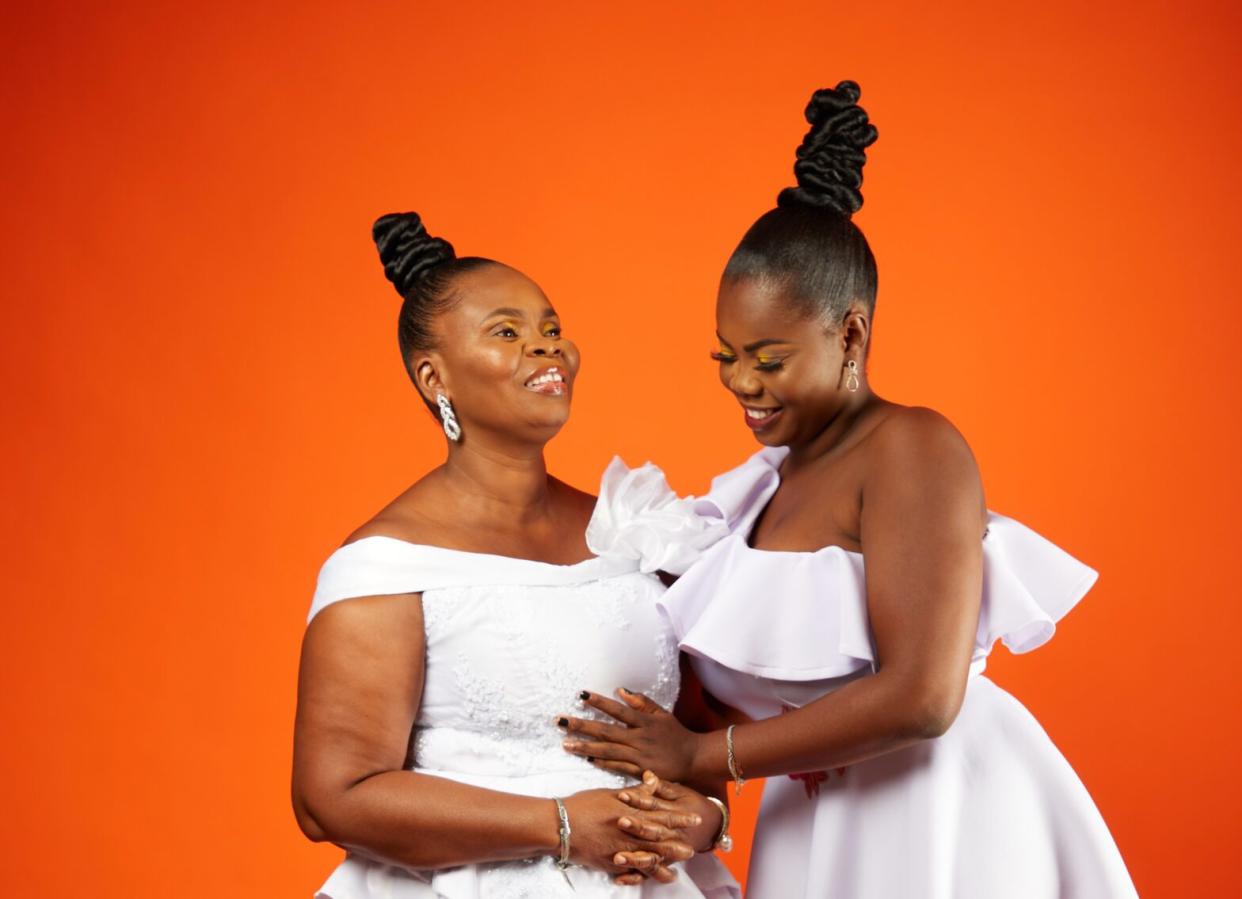 Two Black women in white wedding dresses on orange background