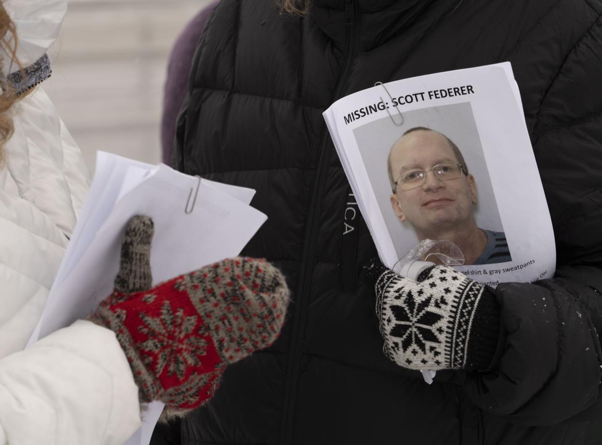 People hand out posters during a vigil Sunday held for the disappearance of Scott Federer at the bus stop where he was last seen.