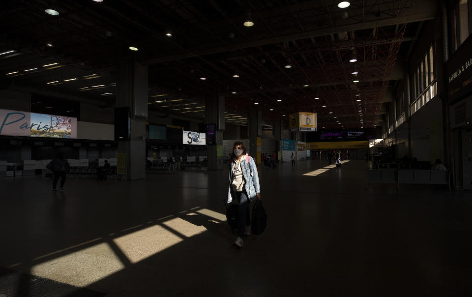 A few people walk through an empty corridor inside the Sao Paulo International Airport in Guarulhos, Brazil, Wednesday, May 27, 2020. According to the airport administration, Brazil's busiest airport has had an average reduction of 85% in flights, due to the COVID-19 pandemic. (AP Photo/Andre Penner)