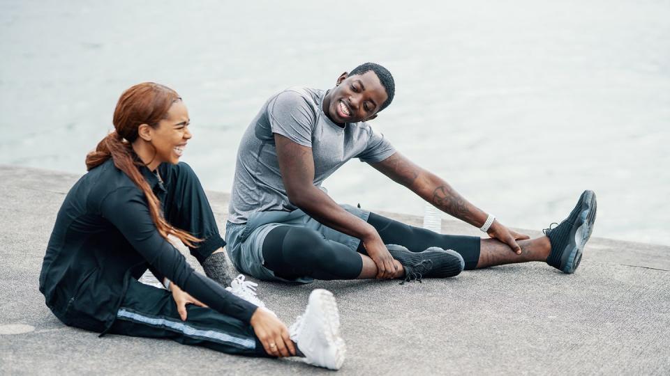 young couple stretching together before or after running or jogging along the coast