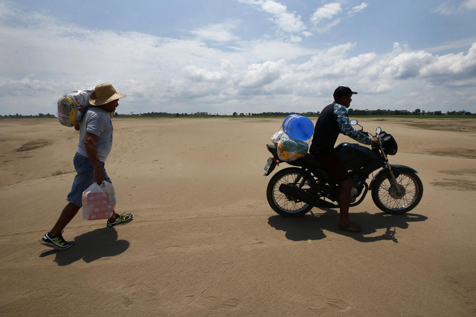 FILE - Residents of a riverside community carry food and containers of drinking water after receiving aid due to the ongoing drought in Careiro da Varzea, Amazonas state, Brazil, Tuesday, Oct. 24, 2023. On Tuesday, the municipality distributed emergency kits using an improvised barge originally designed to transport cattle. (AP Photo/Edmar Barros, File)
