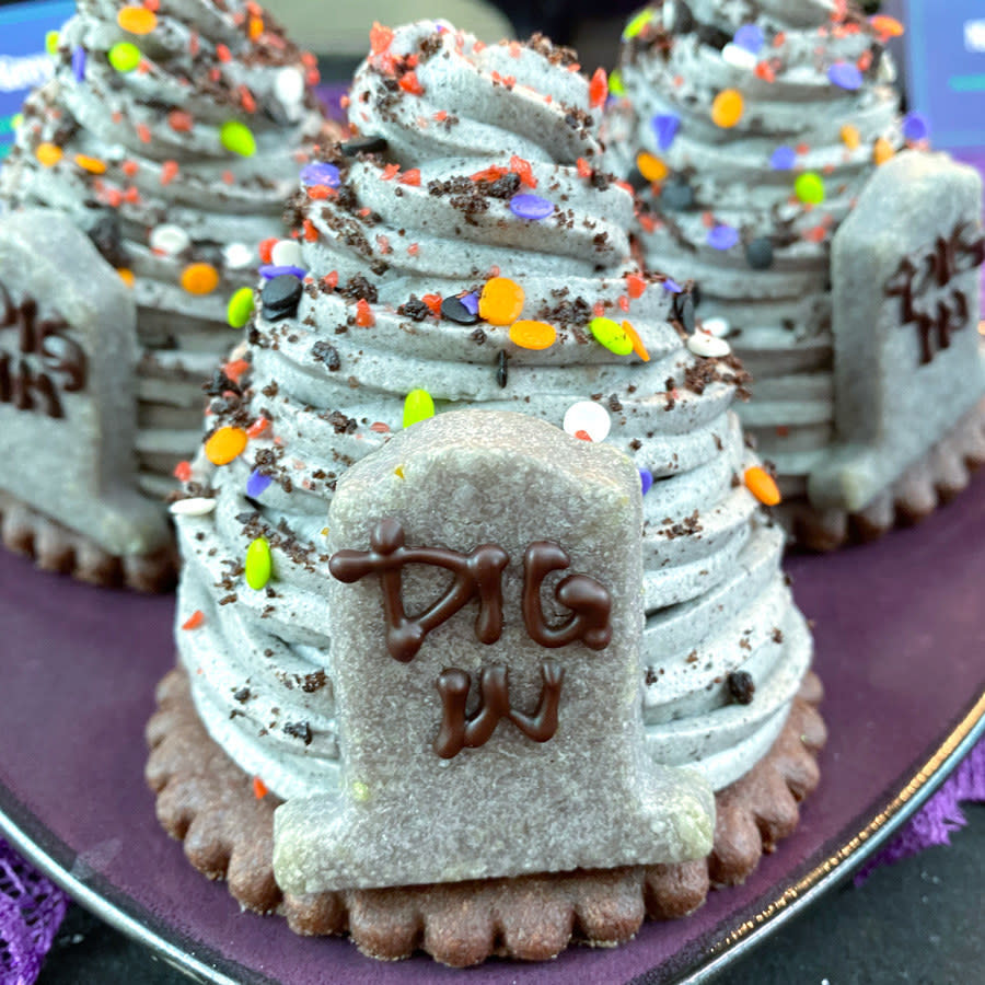 A swirl of grey mousse on top of a round cookie, and an cookie on top of it all in the shape of a tombstone that says "dig in"