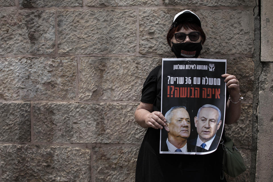 A woman wears a mask for protection against the spread of the coronavirus holds a sign that reads: 'a government with 36 ministers? Where is the shame?'" in Jerusalem, Sunday, May 3, 2020. Israel's high court heard petitions Sunday that seek to block Prime Minister Benjamin Netanyahu from forming a government because he has been charged with serious crimes. (AP Photo/Tsafrir Abayov)