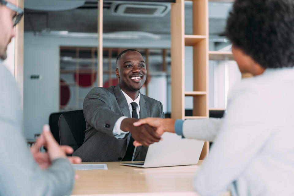 Business people handshaking across the table during a meeting in modern office. Group of business persons in business meeting. Three entrepreneurs on meeting in board room. Corporate business team on meeting in the office.