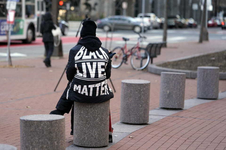 A lone demonstrator sits on a cement barrier, Thursday, Dec. 2, 2021, at the Hennepin County Government Center in Minneapolis as jury selection enters the third day for former suburban Minneapolis police officer Kim Potter. Potter, who is white, is charged with manslaughter in the April 11 shooting of Wright, a 20-year-old Black motorist, following a traffic stop in Brooklyn Center. (AP Photo/Jim Mone)