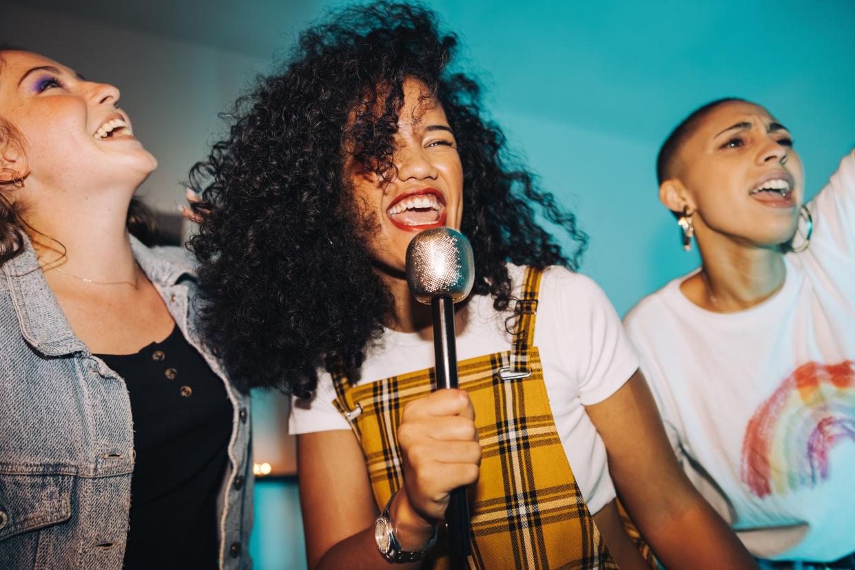 Karaoke time. Vibrant young woman singing into a microphone while partying with her friends at night.  Group of happy female friends having a good time together on the weekend.