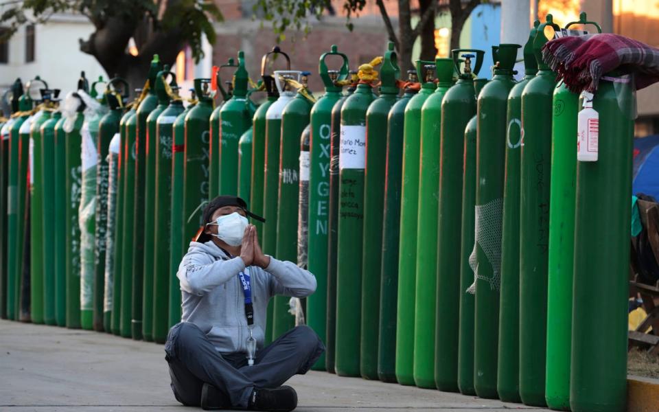 A man prays after waiting three days next to an empty oxygen tank for his uncle who has Covid-19 outside a refill shop in Callao, Peru - AP