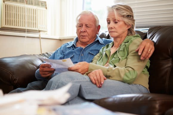 Serious senior couple seated side by side on a sofa and looking at paperwork