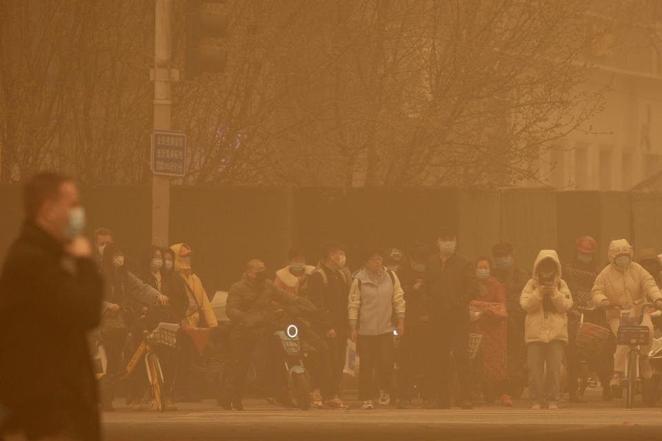 People wait to cross an intersection amid a sandstorm during the morning rush hour in Beijing, Monday, March 15, 2021. The sandstorm brought a tinted haze to Beijing's skies and sent air quality indices soaring on Monday. (AP Photo/Mark Schiefelbein)