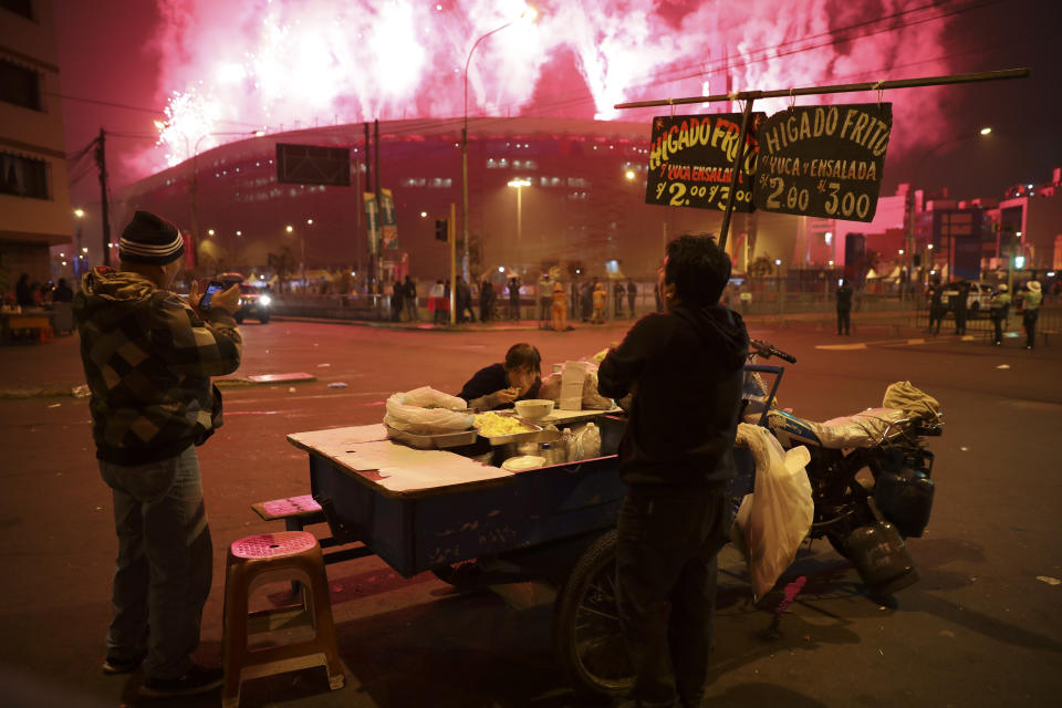 Vendors at a food stand watch fireworks exploding over the National stadium during the closing ceremony of the Pan American Games in Lima, Peru, Sunday, Aug. 11, 2019. (AP Photo/Rodrigo Abd)