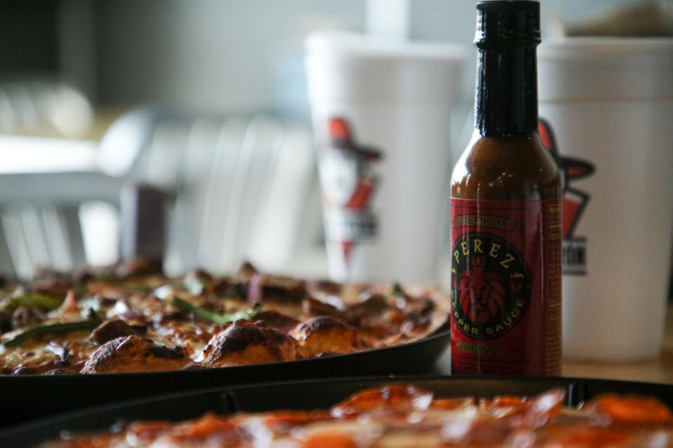 A bottle of Pérez Pepper Sauce, created by Grammy Award-winning guitarist Chris Pérez, sits at a table with three pizzas that feature the hot sauce at Corpus Christi's new Pizza Patrón on Thursday.