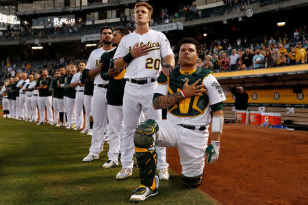 Bruce Maxwell of the Oakland Athletics kneels as teammate Mark Canha places his hand on Maxwell's shoulder during the singing of the national anthem in Oakland. REUTERS/Stephen Lam