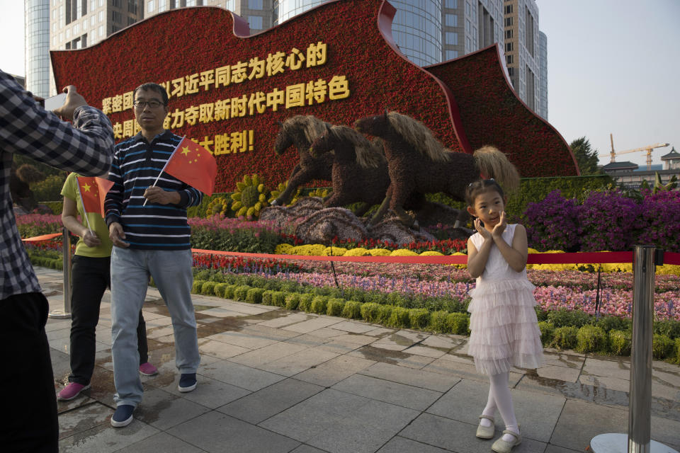 In this Saturday, Sept. 28, 2019, photo, a child poses for photos near a floral display marking the upcoming 70th anniversary of the Founding of the People's Republic of China in Beijing. Chinese President Xi Jinping has an ambitious goal for China: to achieve "national rejuvenation" as a strong and prosperous nation by 2049, which would be the 100th anniversary of Communist Party rule. One problem: U.S. President Donald Trump wants to make the United States great again too. (AP Photo/Ng Han Guan)