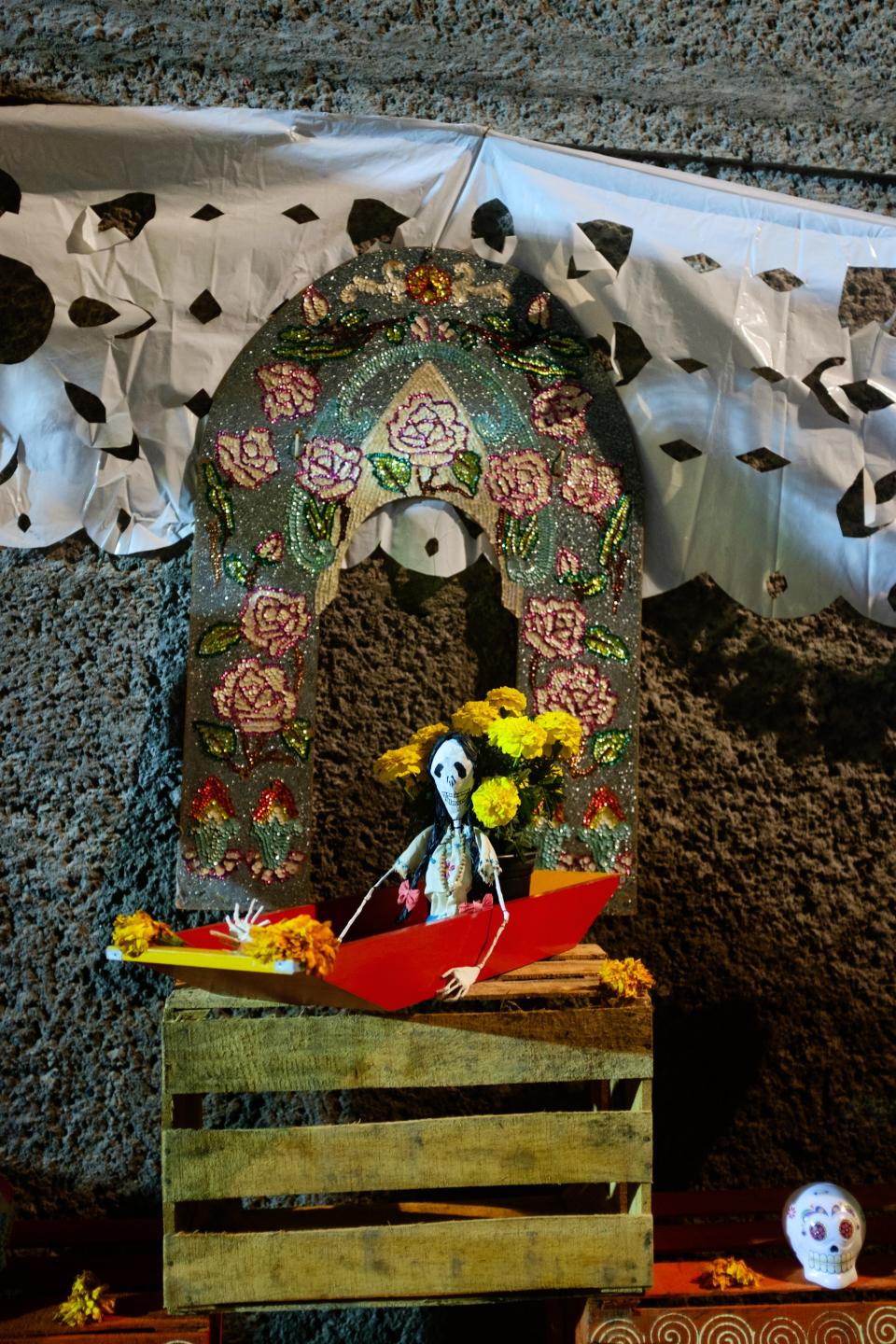 A representative Xochimilco ofrenda—the Catrina sits in a trajinera, with the classic arch motif in the background.