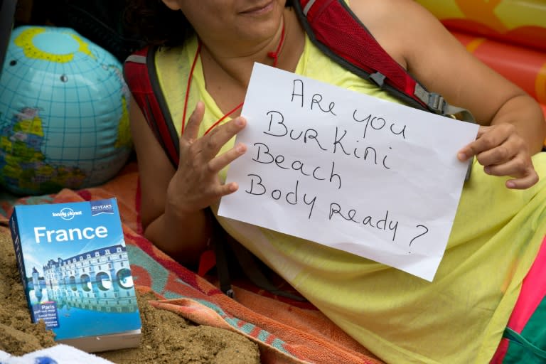 A protester holds a sign as she lies on a beach towel outside the French Embassy in London on August 25, 2016, during a "Wear what you want beach party" to protest the ban on Burkinis on French beaches, and to show solidarity with Muslim women