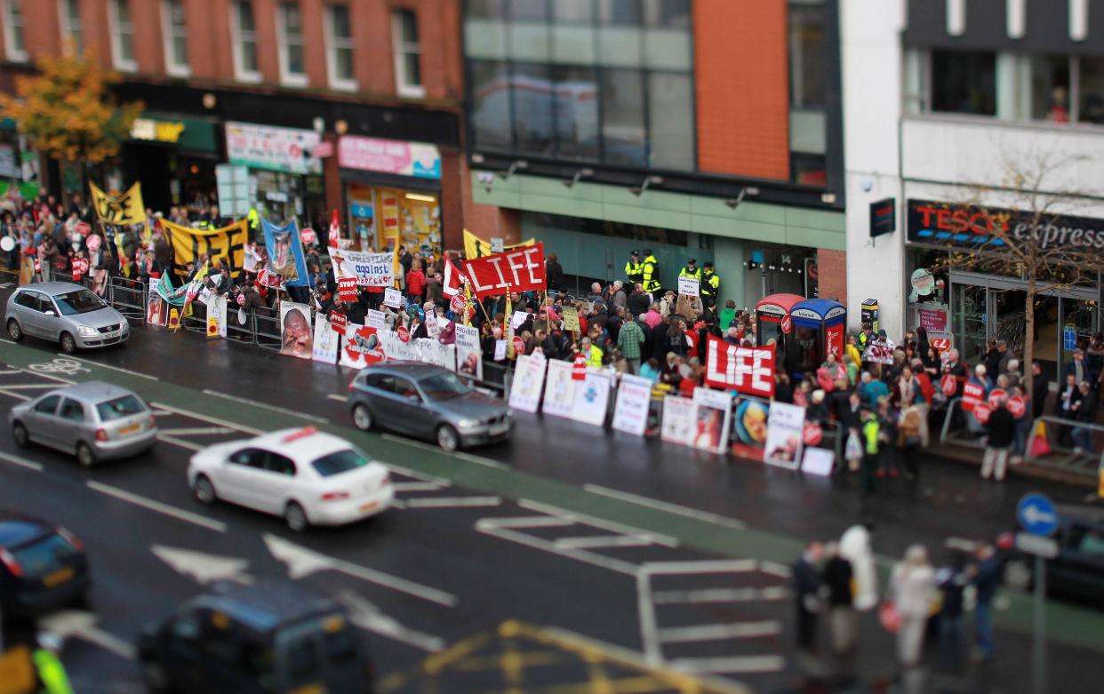 Police stand at the entrance of the Marie Stopes clinic as anti abortion protestors hold up placards outside the first private clinic to offer abortions to women in Belfast, Northern Ireland on October 18, 2012. Dozens of pro-life campaigners protested outside the first abortion clinic in Northern Ireland as it opened to the public. Around 50 protesters brandishing placards saying "Life is precious" and showing photographs of foetuses gathered outside the privately run clinic in an anonymous building in Belfast. AFP PHOTO/ Peter Muhly  -NOTE TO EDITORS THIS PICTURE WAS TAKEN USING A TILT AND SHIFT LENS -        (Photo credit should read PETER MUHLY/AFP via Getty Images)