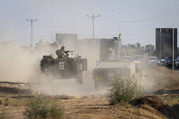 Armoured vehicles travel along a dirt track near the border with Gaza on 12 October 2023 in Kibbutz Re’im, Israel (Getty Images)