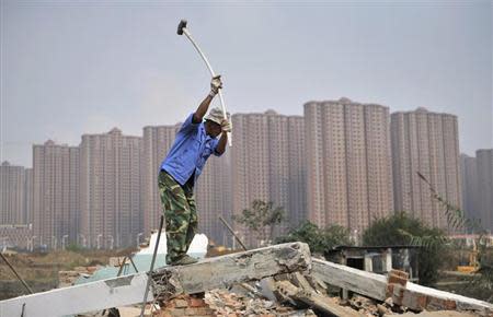 A worker wields a hammer at a demolition site in front of new residential buildings in Hefei, Anhui province, October 19, 2013. REUTERS/Stringer